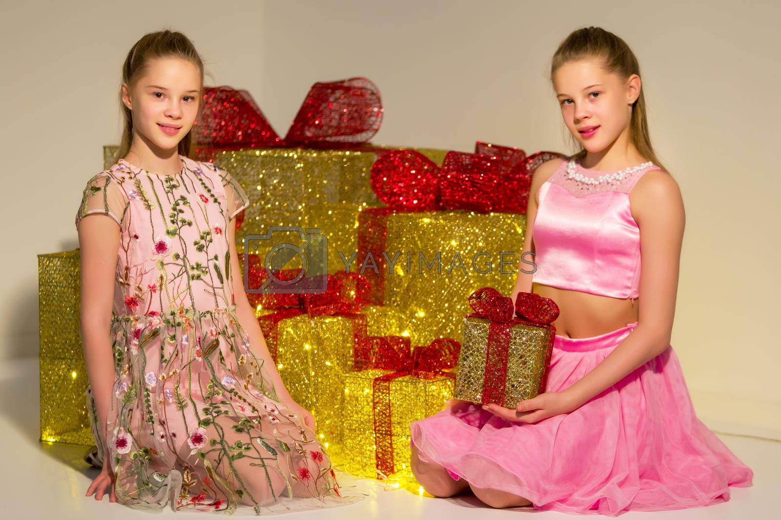 Royalty free image of Twin Sisters Sitting on Floor on Background Piled Golden Gift Boxes. by kolesnikov_studio