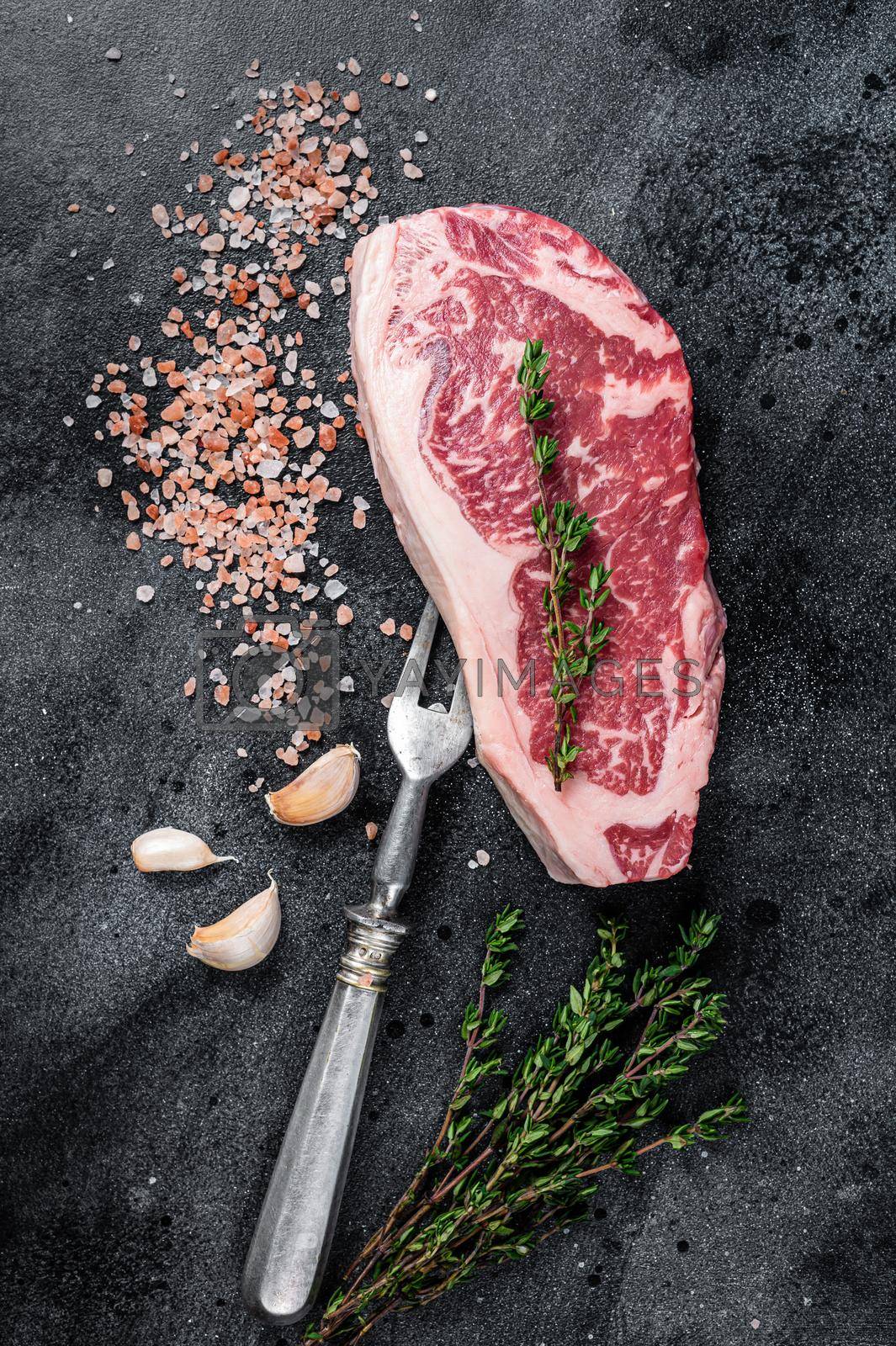 Royalty free image of Raw striploin steak on a butcher table with salt and thyme. Black background. Top view by Composter
