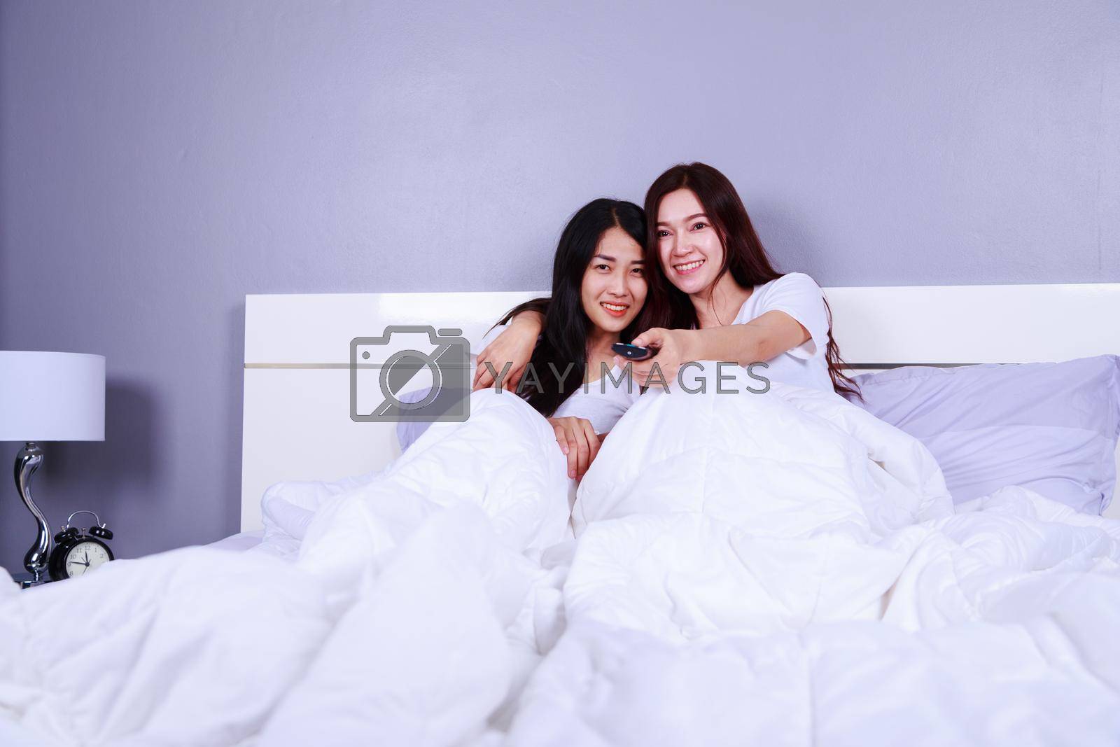Royalty free image of two best friends watching tv with remote on bed in bedroom by geargodz