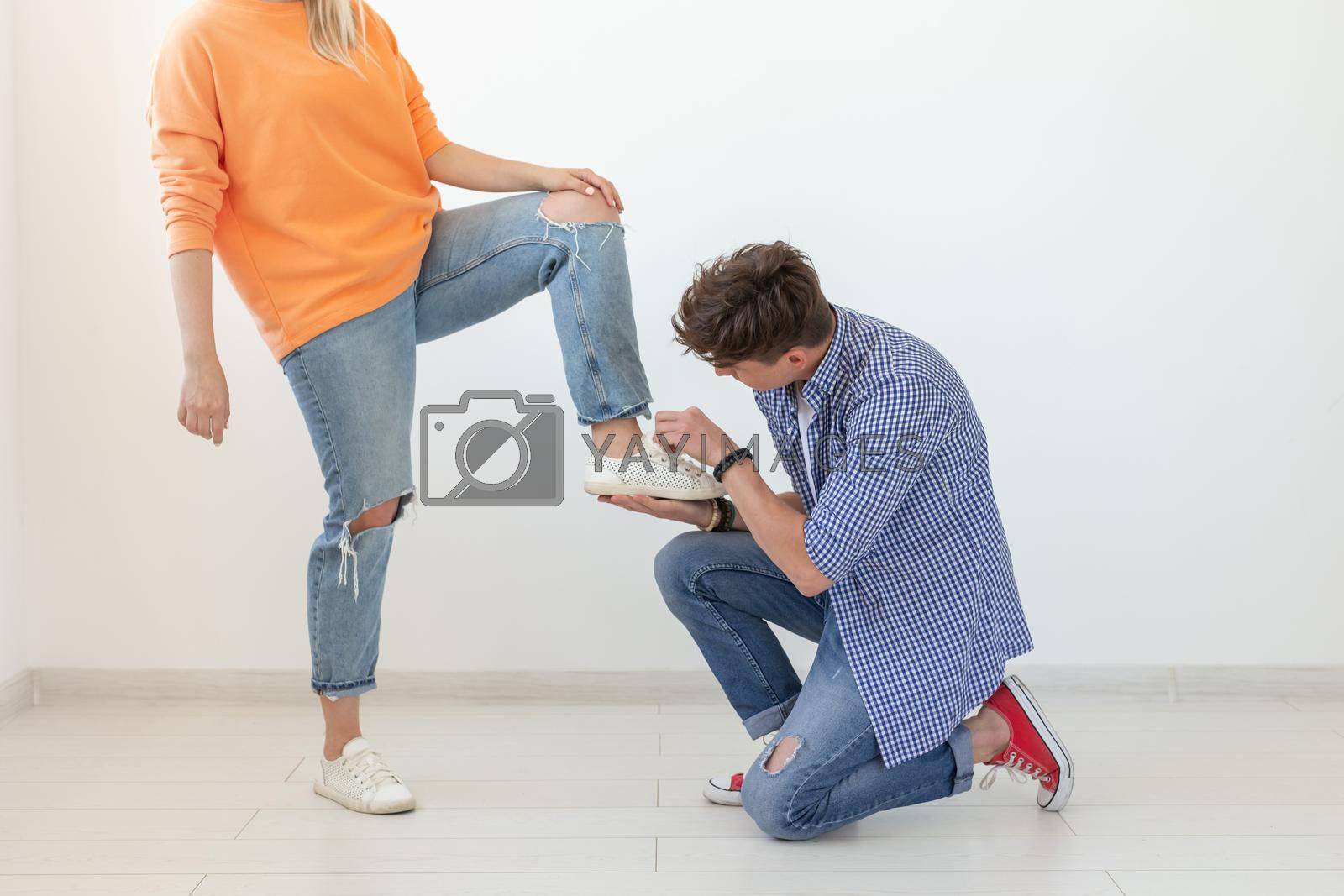 Royalty free image of Young man is kneeling and reverently tying shoelaces to his domineering unidentified woman posing on a white background. Concept of dominant relationships. by Satura86
