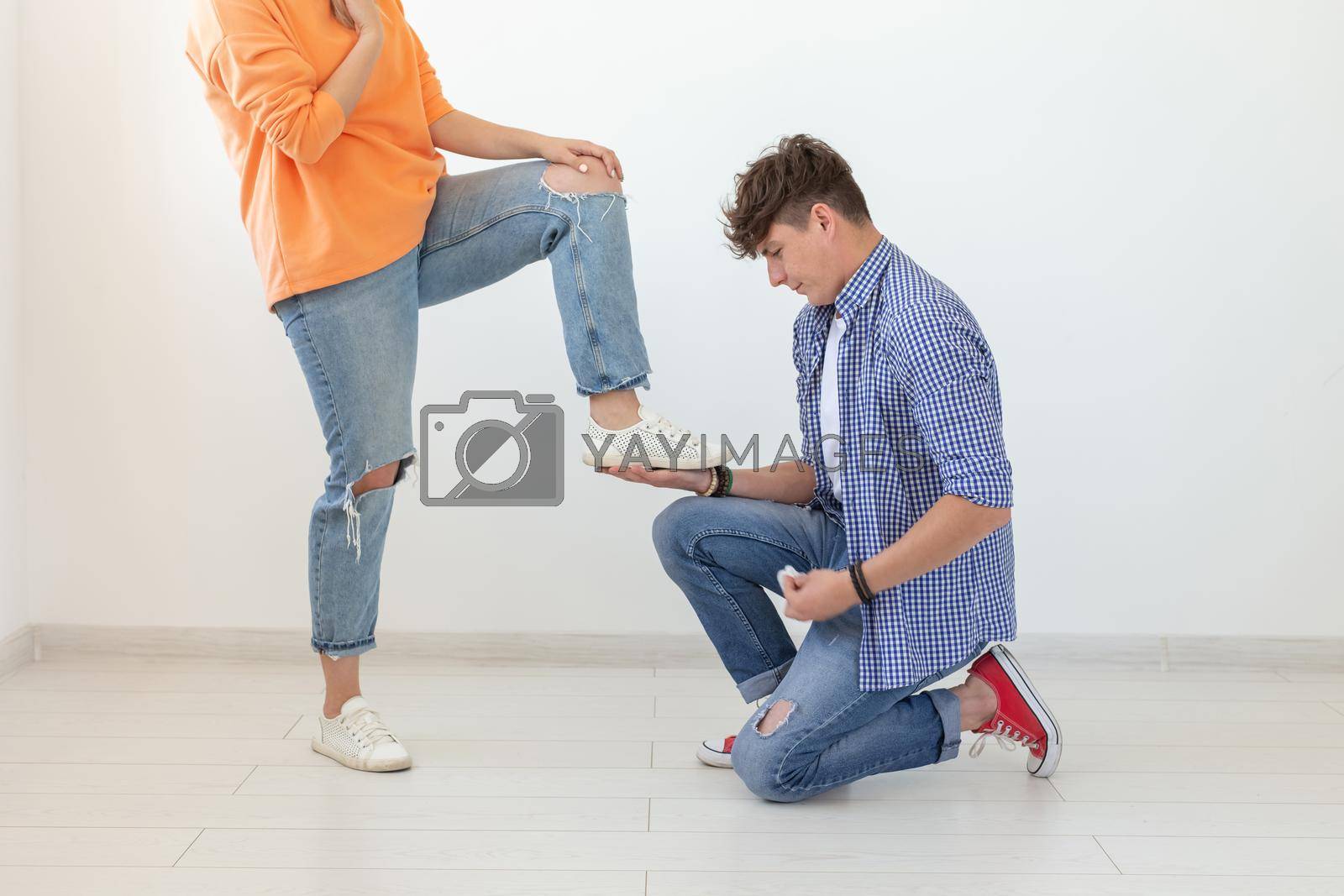 Royalty free image of Young man is kneeling and reverently tying shoelaces to his domineering unidentified woman posing on a white background. Concept of dominant relationships. by Satura86