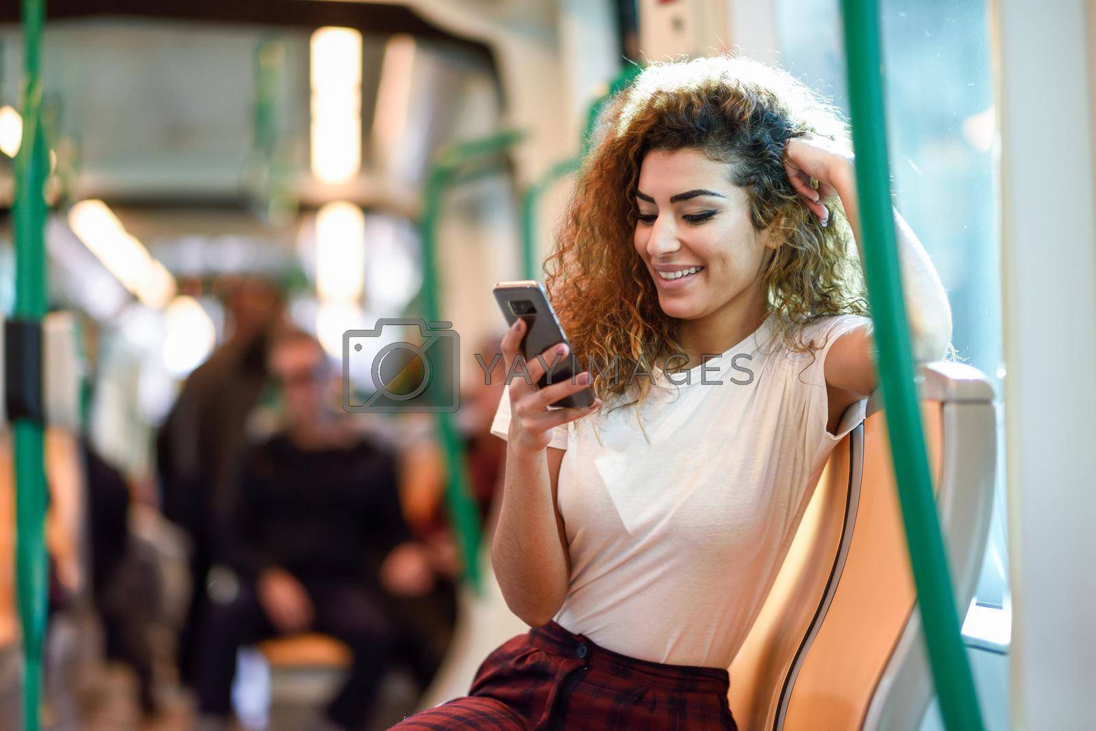 Young Arab woman inside subway train looking at her smart phone. Female in casual clothes.