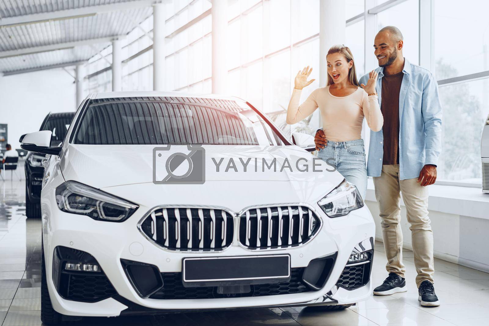 Royalty free image of Young happy couple choosing a car in car dealership by Fabrikasimf