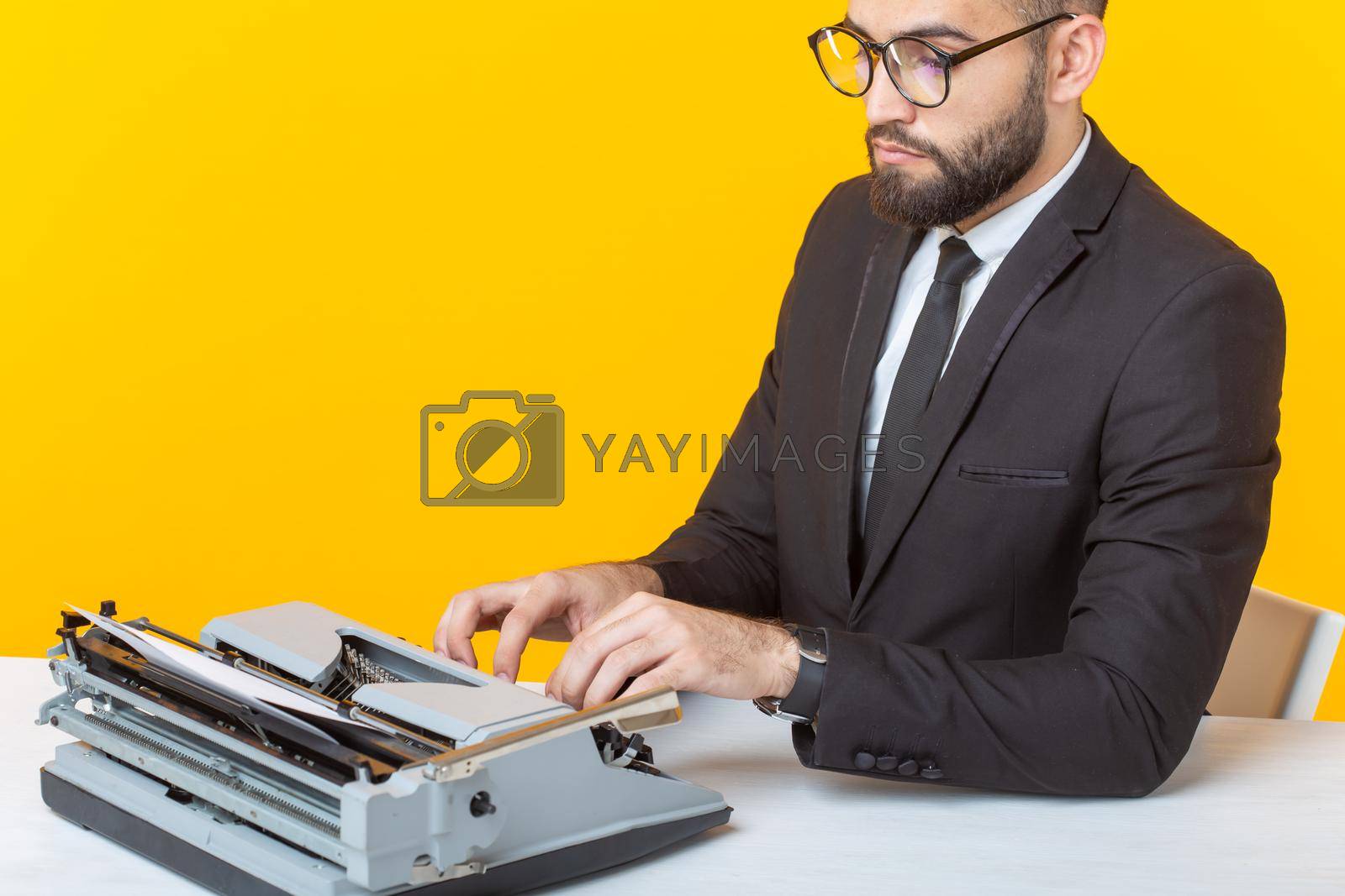 Royalty free image of Side view of a young charming male businessman in formal attire and glasses typing on a typewriter text. Concept of business affairs and ideas. by Satura86