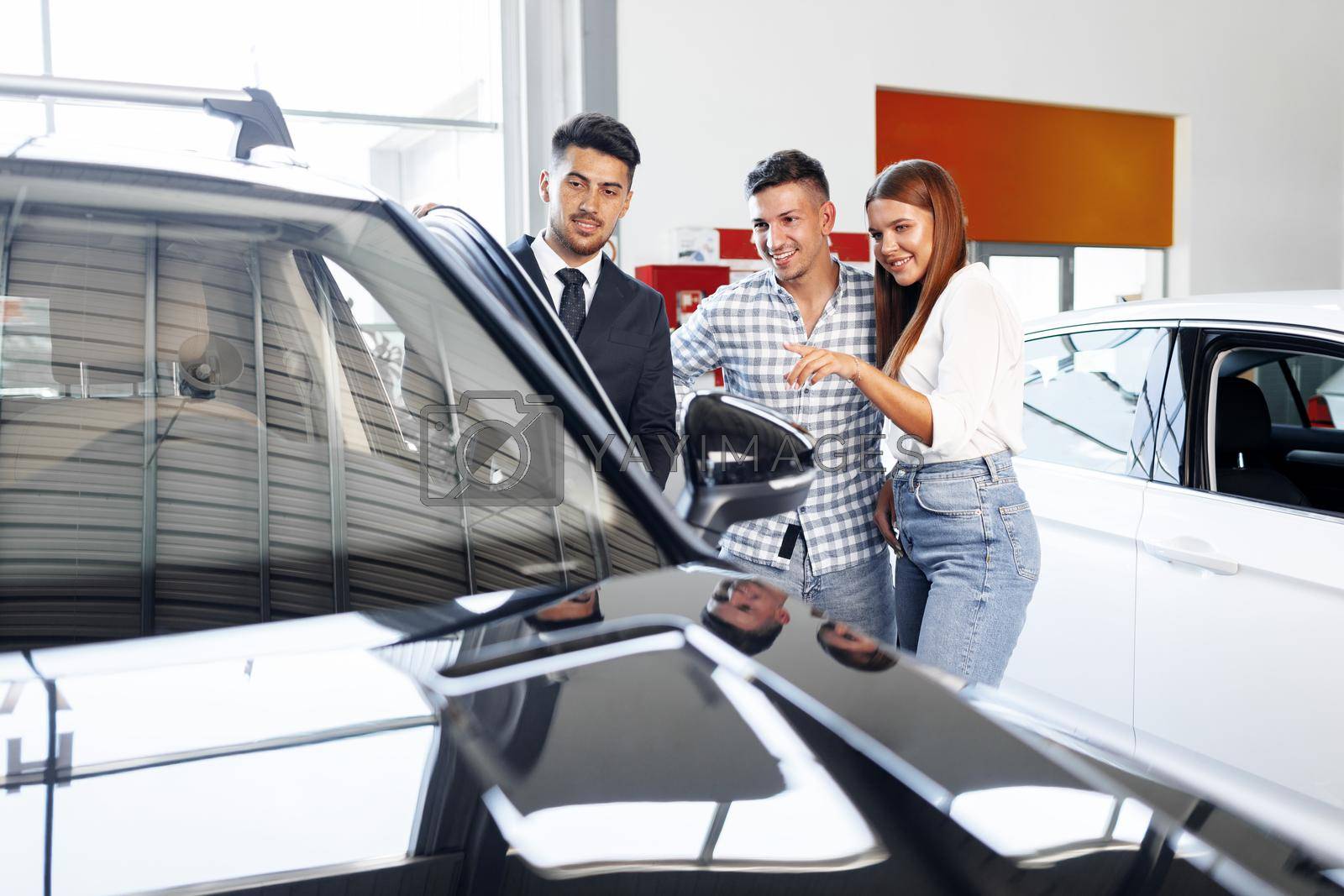 Royalty free image of Young couple choosing a car at the dealership with manager helping by Fabrikasimf