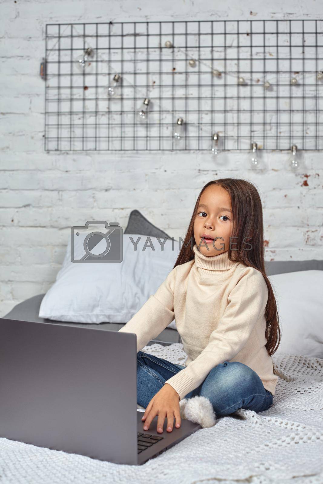 Royalty free image of Cute little girl girl feeling amusing while watching cartoons on a laptop sitting on bed by nazarovsergey