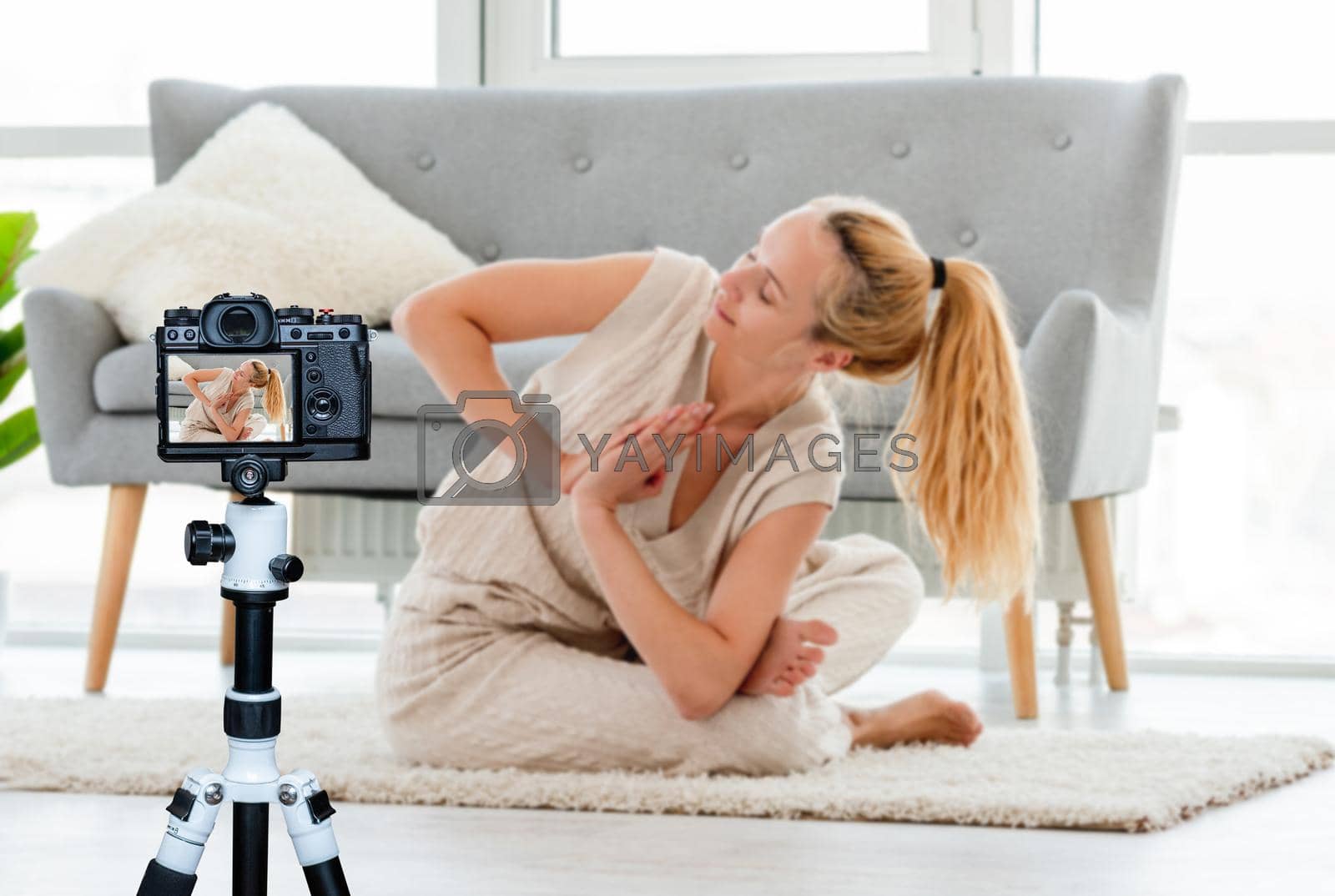 Blond girl sitting in yoga asana on the floor in the room with sunlight. Home stretching workout. Blogger profession. Shooting with a camera for a blog