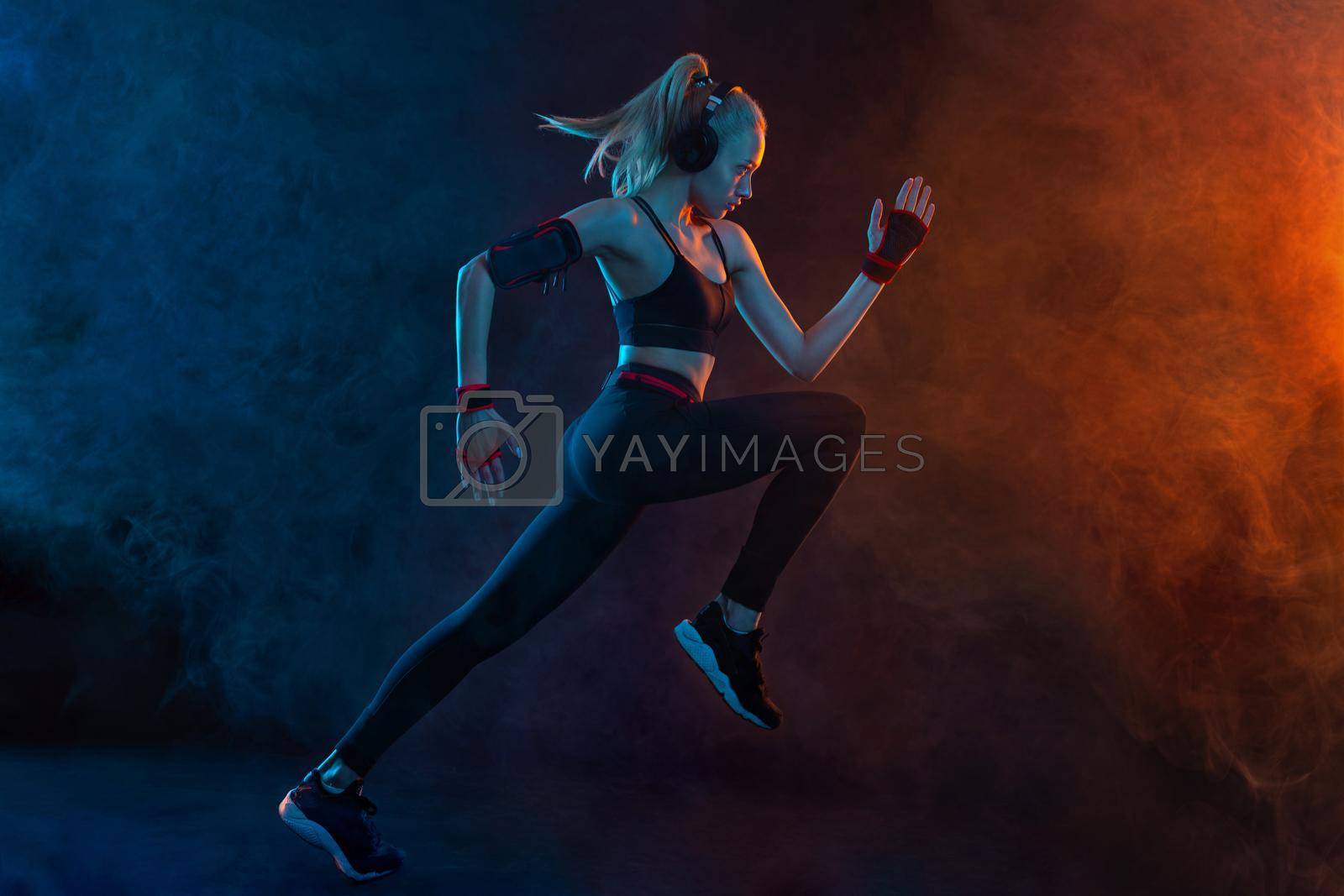 Sprinter run. Strong athletic woman running on black background wearing in the sportswear. Fitness and sport motivation. Runner concept