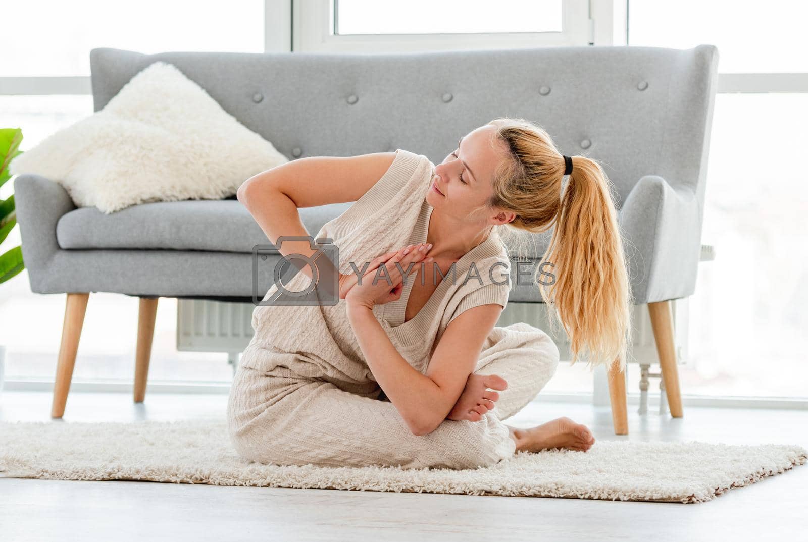 Blond girl sitting in yoga asana on the floor in the room with sunlight. Home stretching workout