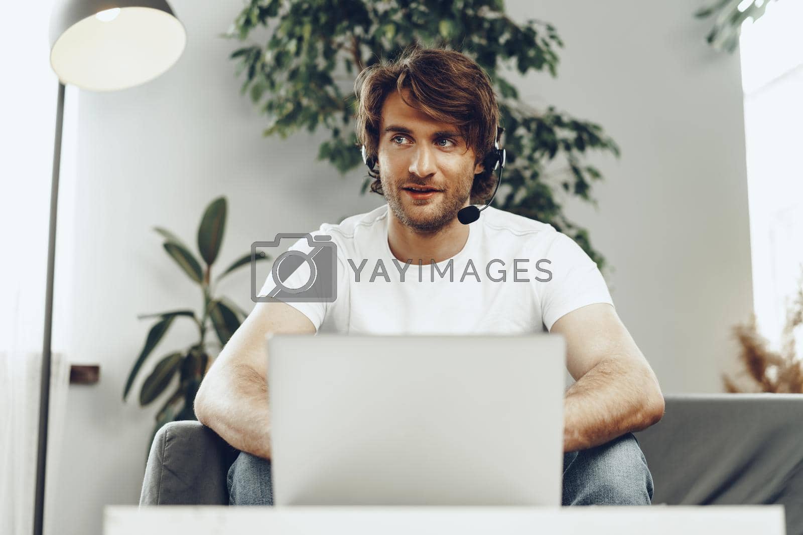 Royalty free image of Young man businessman with headset working on laptop from home by Fabrikasimf