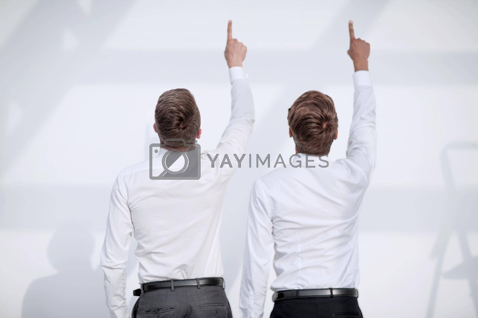 two young people stand with their backs to the camera and point with their thumbs up