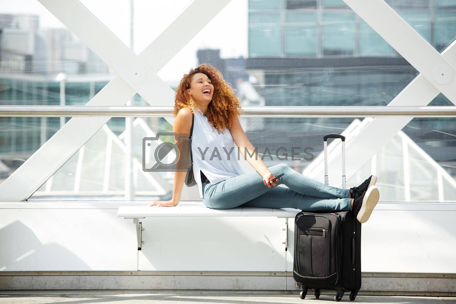 Portrait of happy travel woman sitting with suitcase and cellphone at station