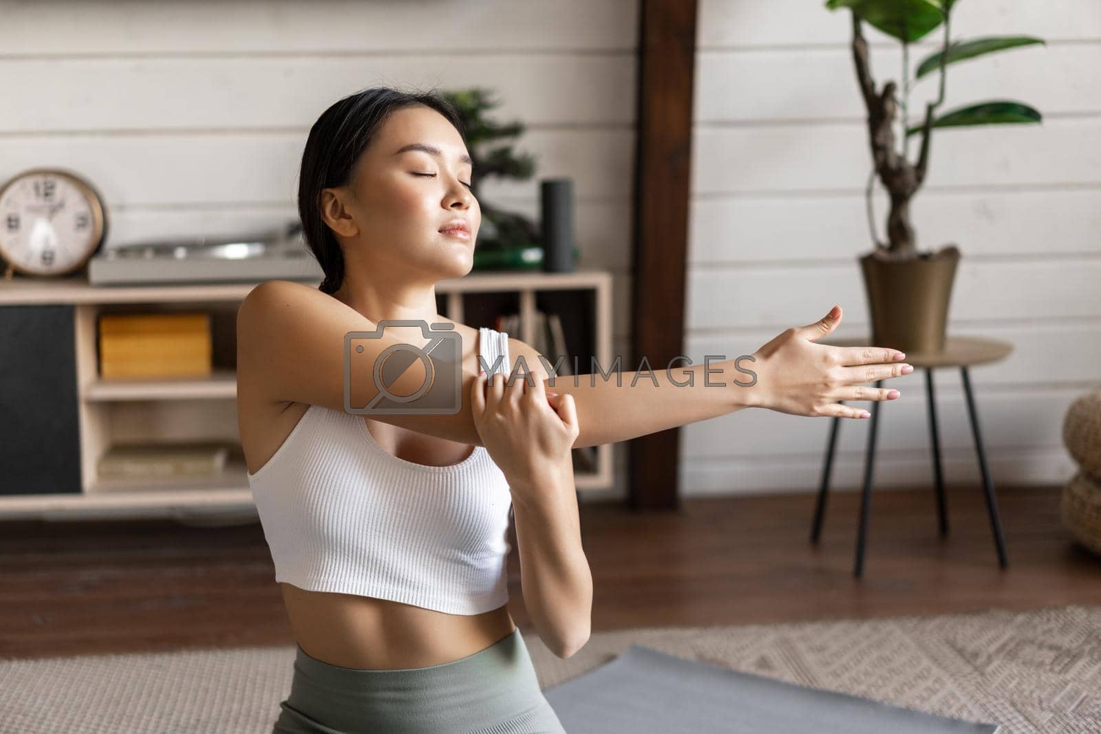 Smiling asian woman doing stretches, fitness workout at home in living room, wearing sport clothing.