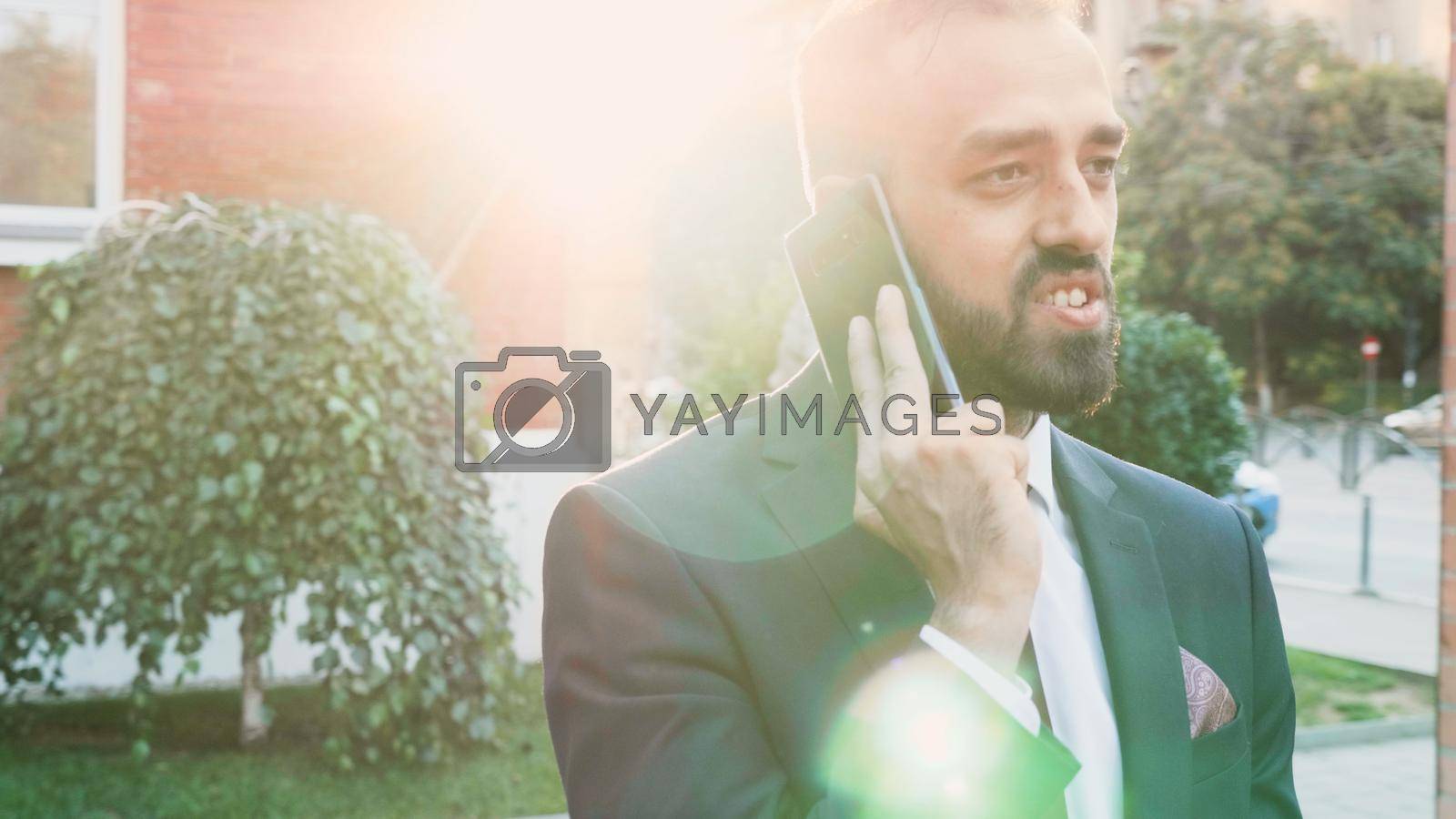 Businessman talking at modern phone discussing financial company with remote manager explaoning marketing strategy. Entrepreneur man standing outside in front on startup corporate office