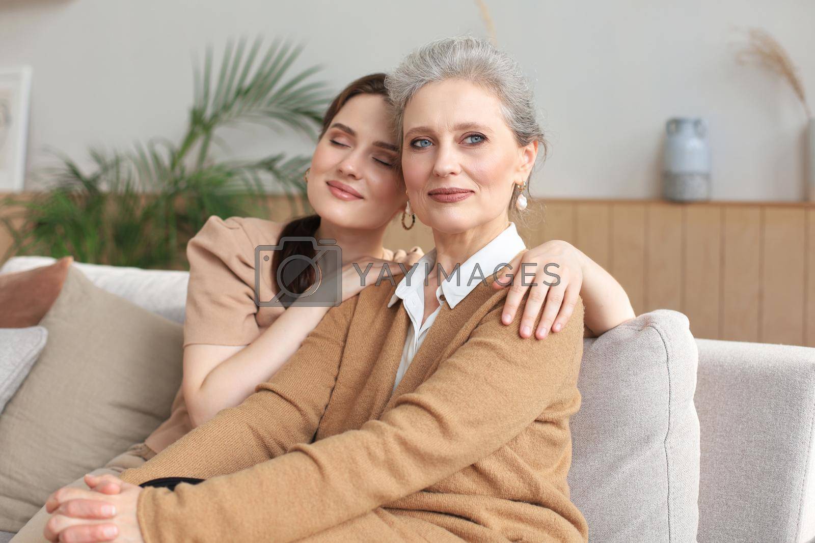 Royalty free image of Portrait of old mother and mature daughter hugging at home. Happy senior mom and adult daughter embracing with love on sofa. by tsyhun
