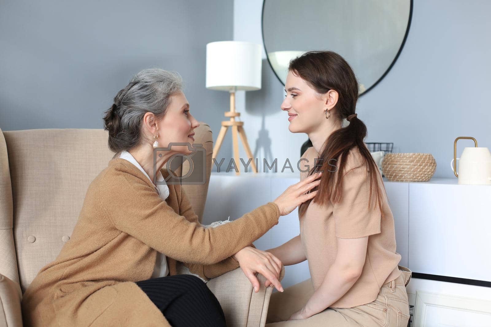 Royalty free image of Happy elderly middle mother sitting on chair touching a strand of daughter's hair, looking each other, trusted relations. Family concept. by tsyhun