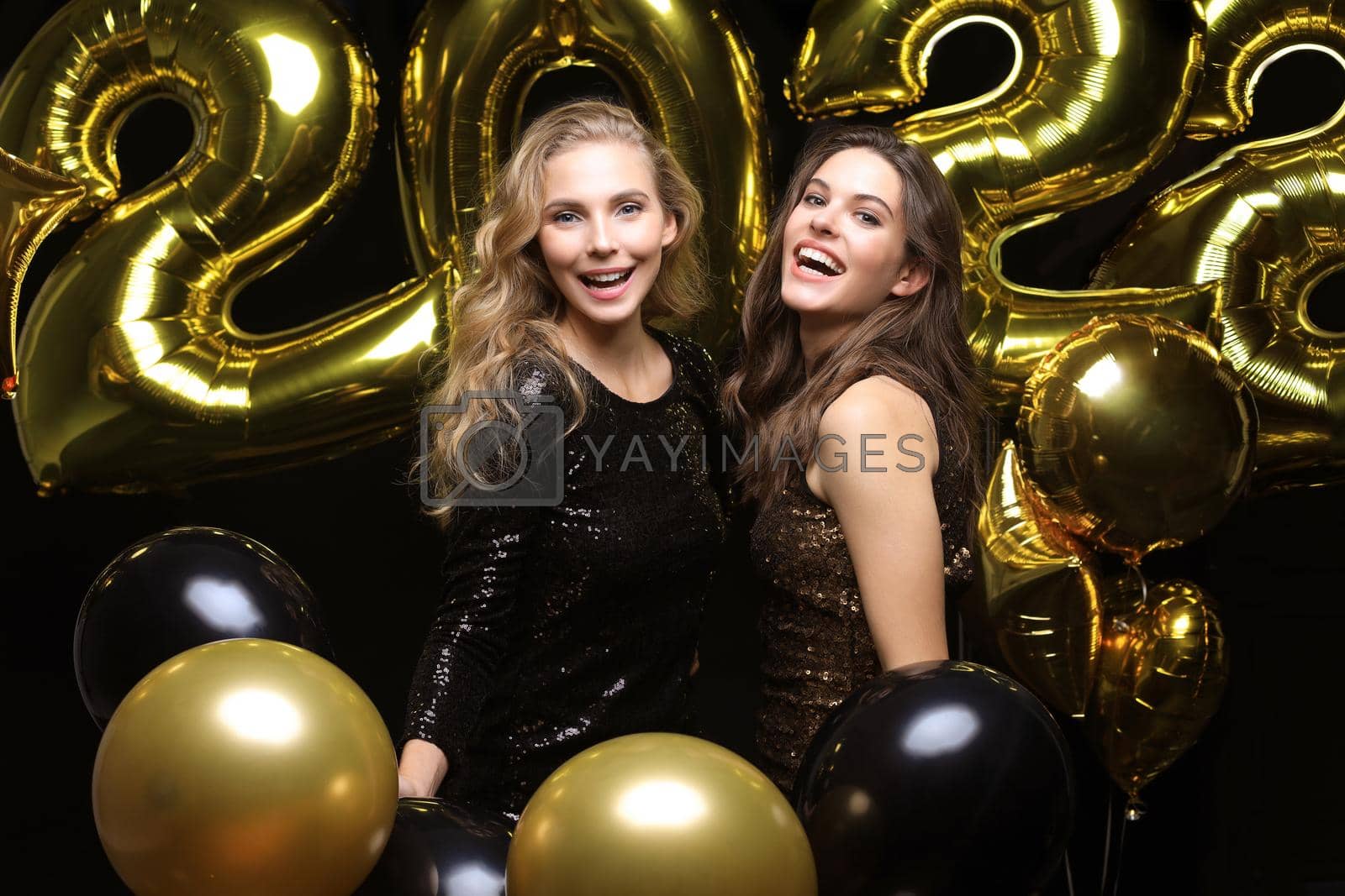 Royalty free image of Happy gorgeous girls in stylish sexy party dresses holding gold 2022 balloons, having fun at Christmas or New Year's Eve Party. by tsyhun