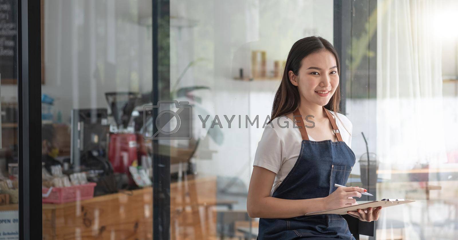 Royalty free image of Cheerful smiling young Asian woman entrepreneur at coffee shop counter with order list by nateemee