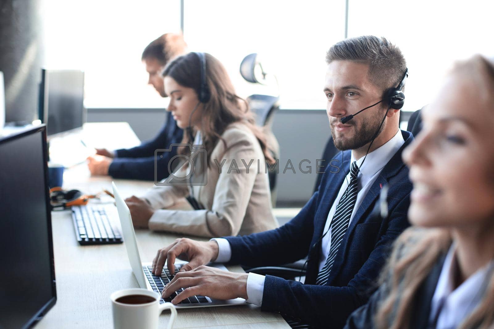 Royalty free image of Portrait of call center worker accompanied by his team. Smiling customer support operator at work. by tsyhun