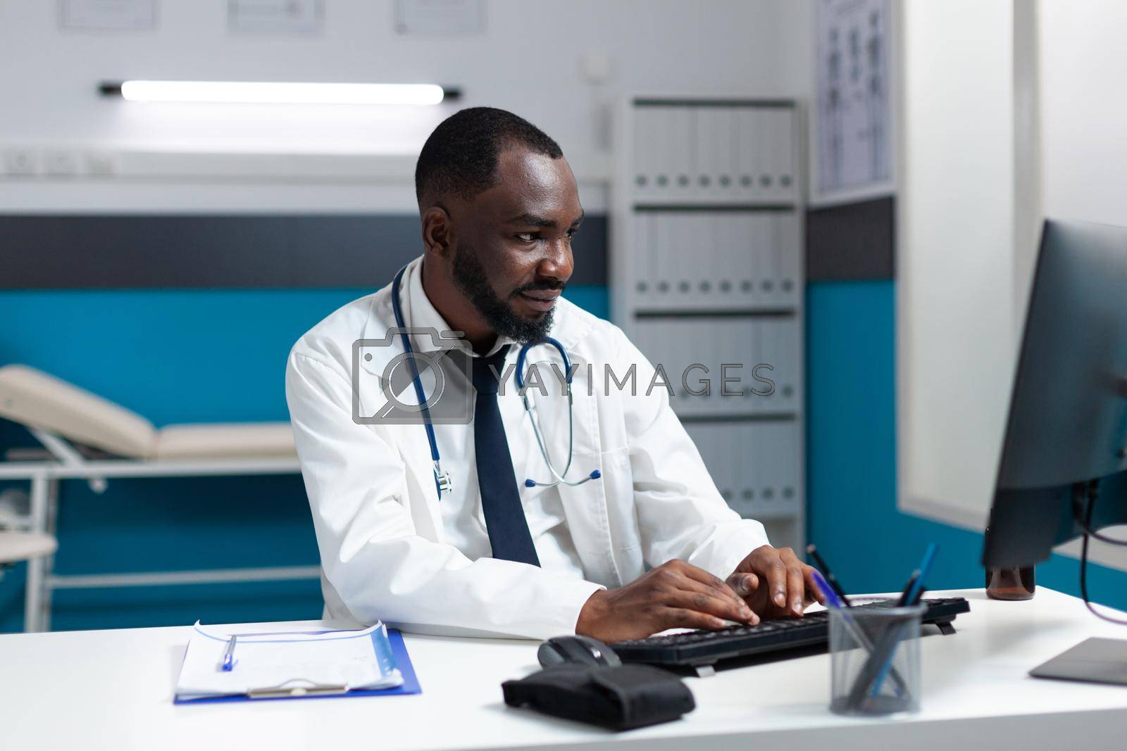 African american therapist doctor typing healthcare treatment on computer after analyzing sickness symptoms expertise during clinical consulation. Therapist working in hospital medical office