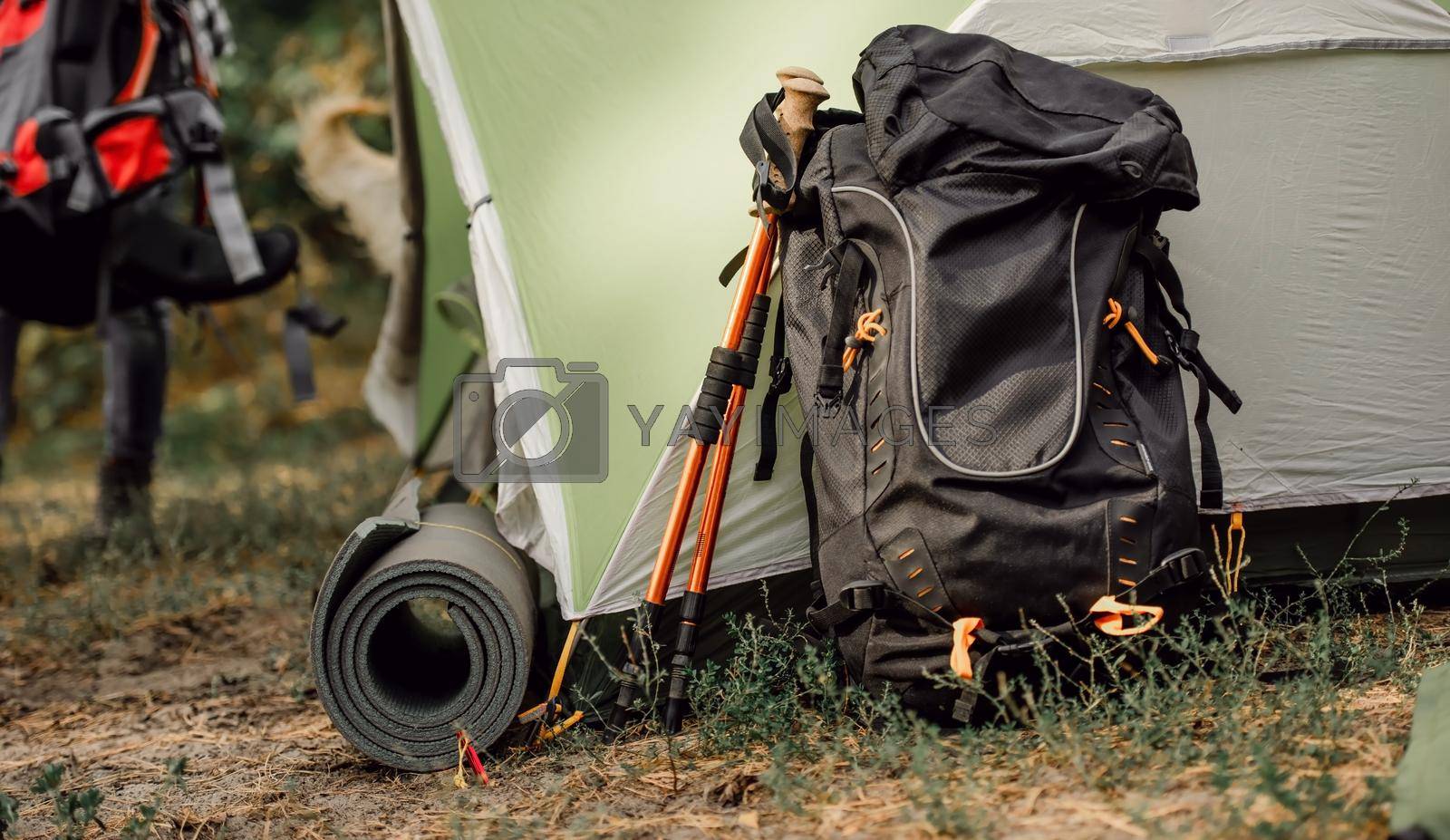 Black backppack and karemat close to tent in camping place in the forest. View on travel touristic hiking equipment outdoor