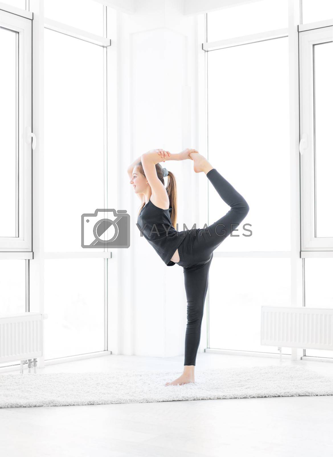 Pretty girl performing king dancer yoga asana indoors
