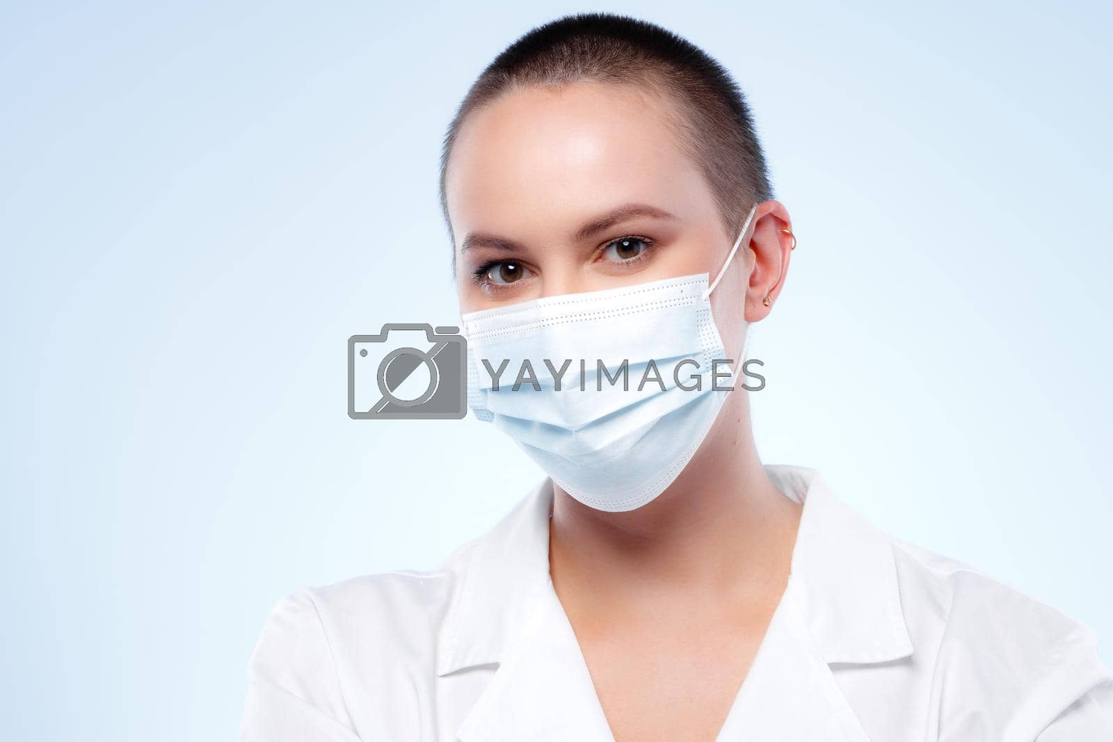 Royalty free image of Short-haired woman doctor in medical gown wearing face mask by Fabrikasimf