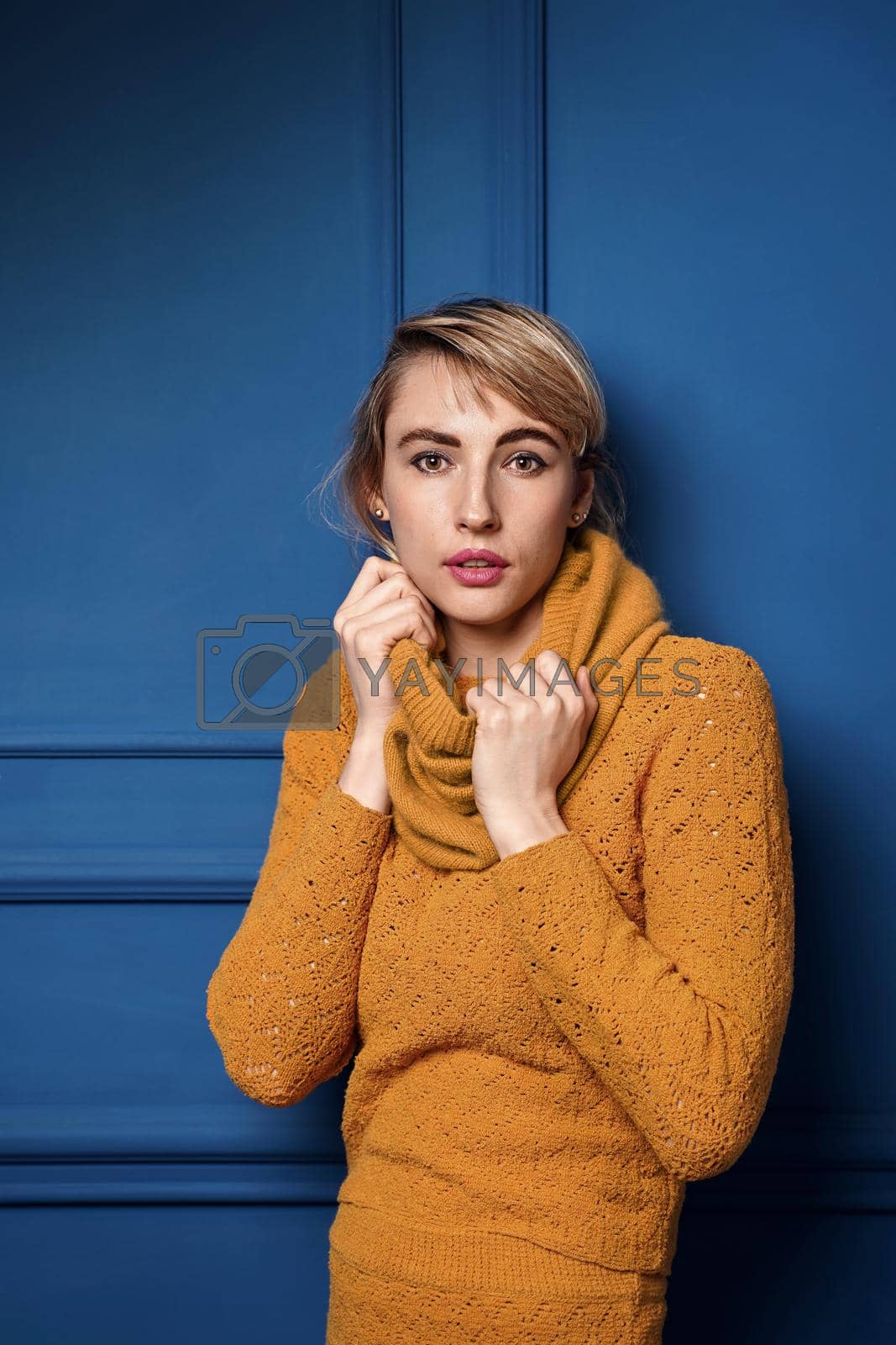Royalty free image of Studio portrait of a young woman in yellow pullover on blue wall background. by berezko