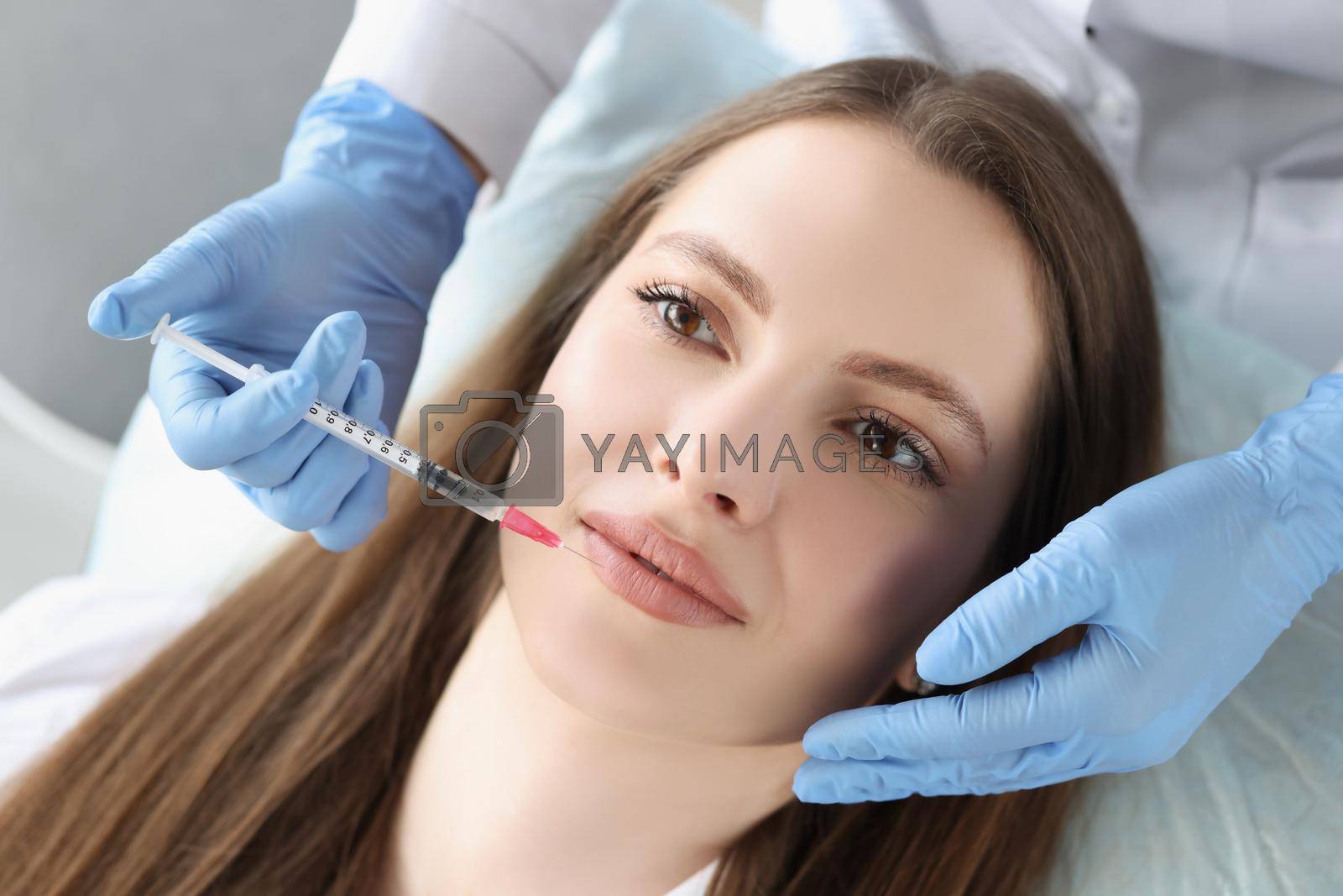 Royalty free image of Young woman gets injection of botox in her lips, cosmetologist using syringe by kuprevich