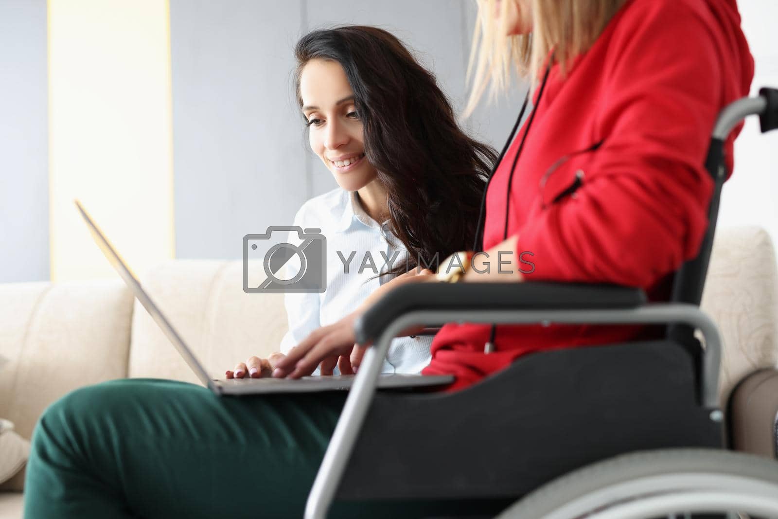 Royalty free image of Best friends spend time together watching movie on laptop, woman in wheelchair hold device on lap by kuprevich