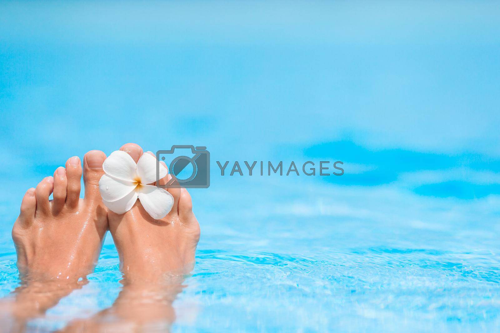 Royalty free image of Feet in blue pool with tropical flower by travnikovstudio