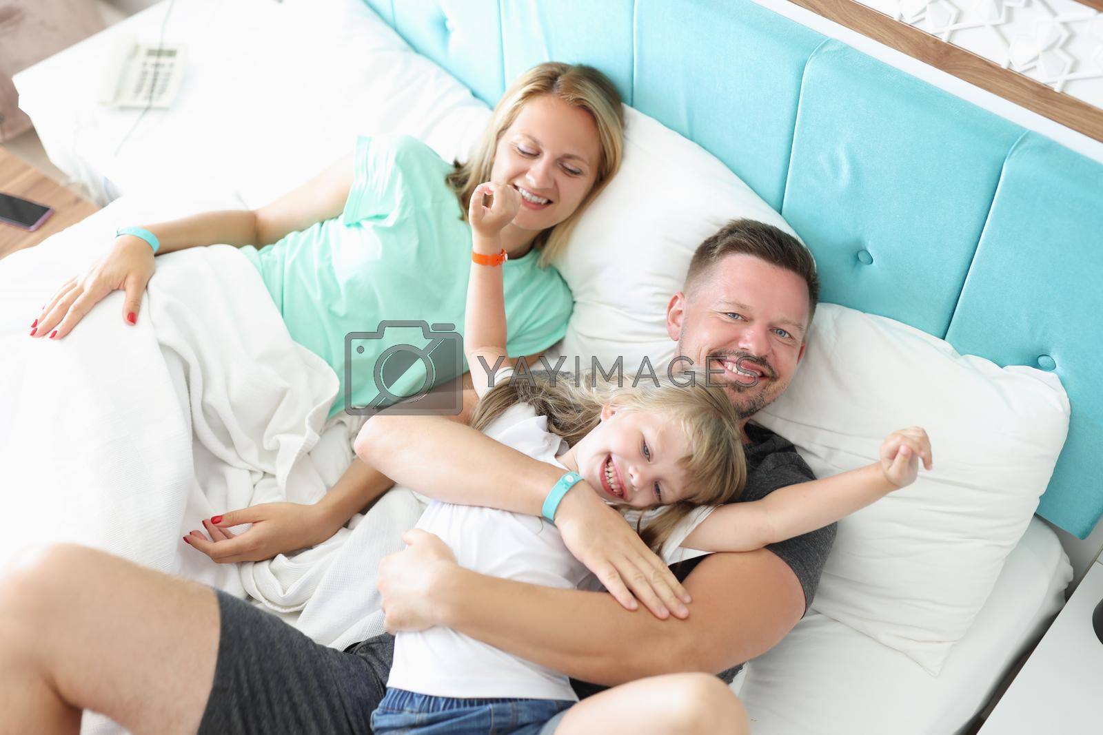 Top view of lovely family rest in bed, father mother and daughter hug in morning. Pure emotion of happiness, quality time. Childhood, parenthood concept