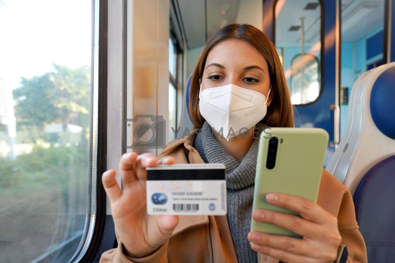 Young woman with FFP2 KN95 protective mask traveling with train paying with her credit card on smart phone for shopping online