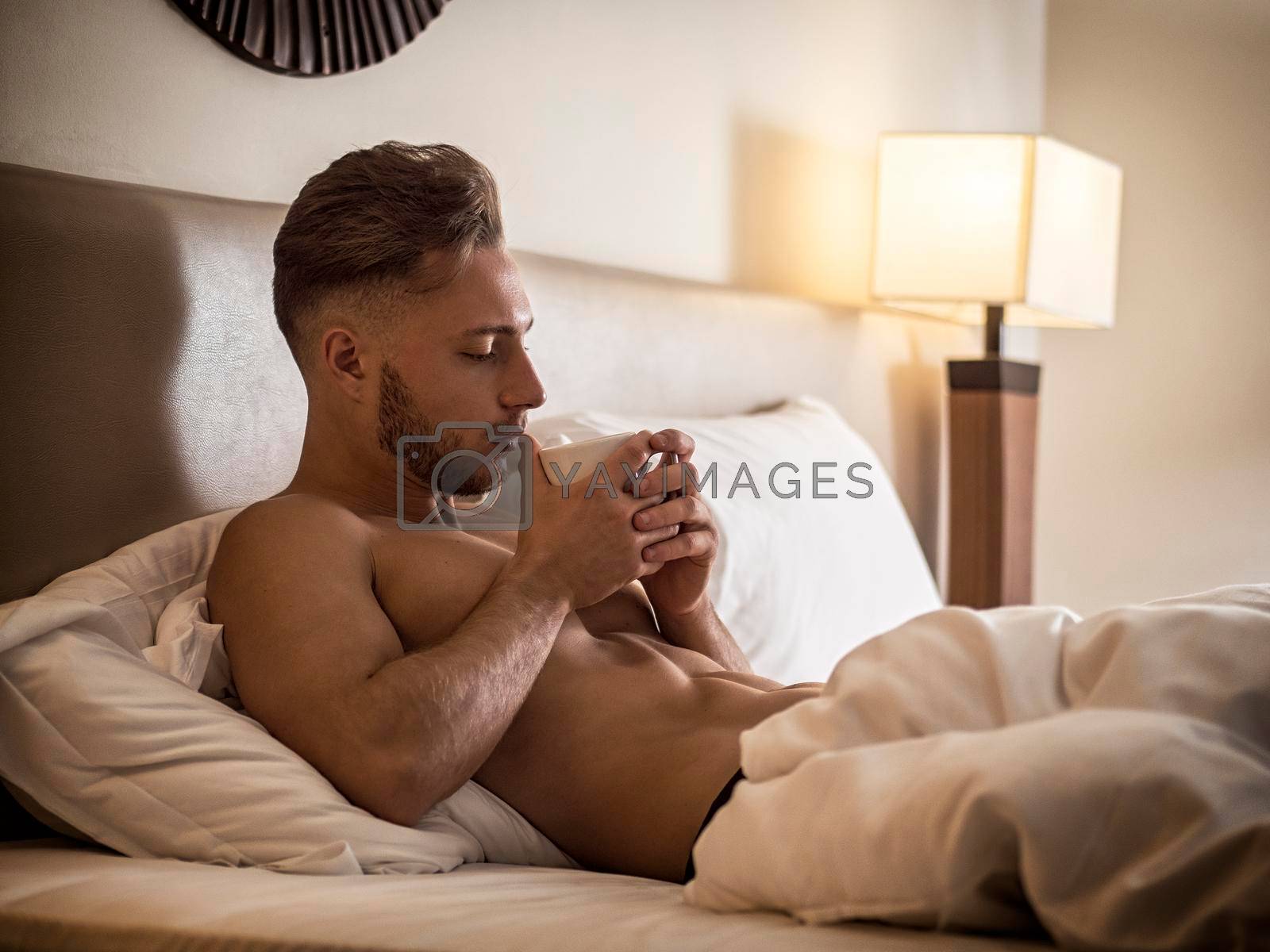 Royalty free image of Sexy naked young man on bed with cup by artofphoto