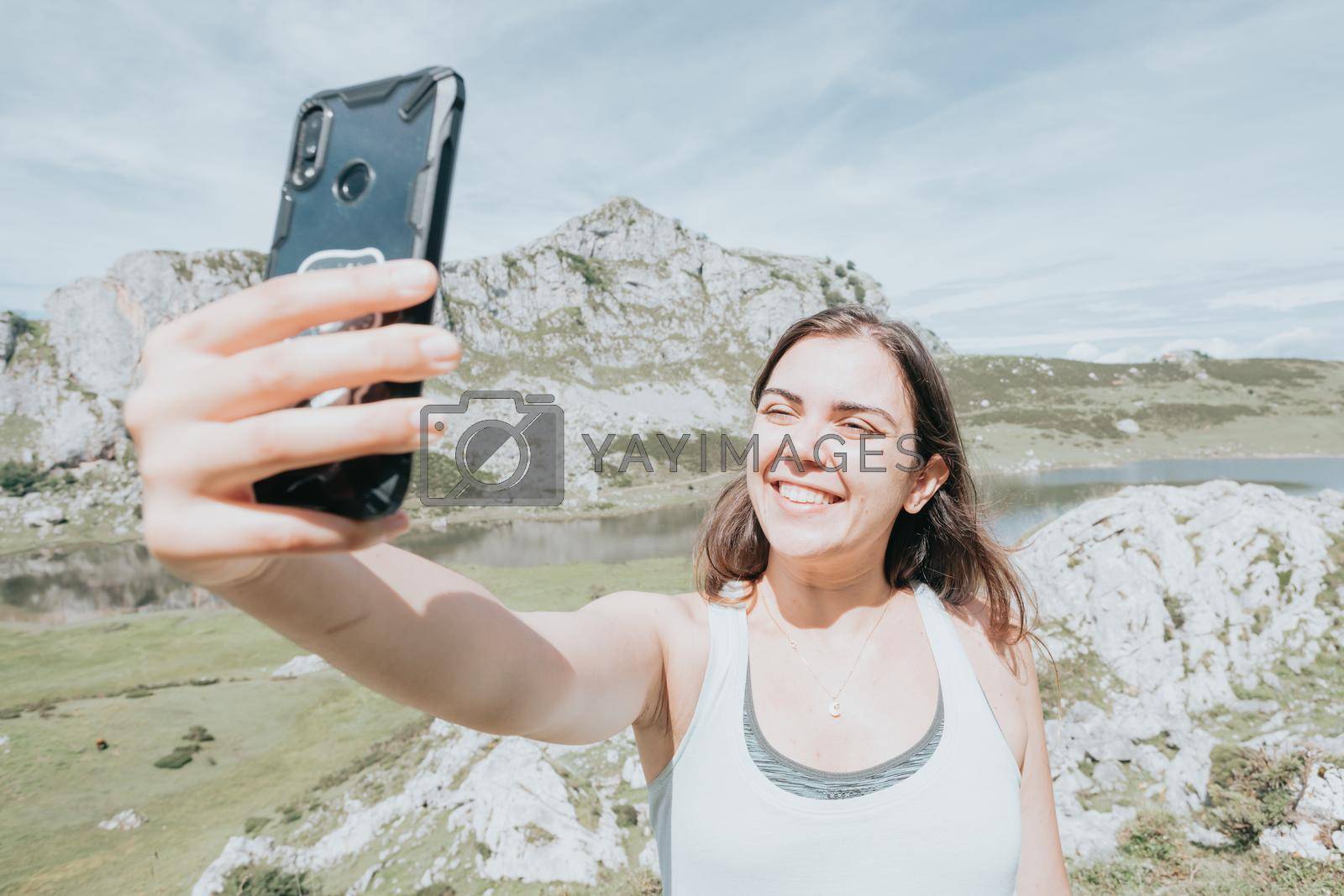 Royalty free image of Portrait of young woman taking selfie smiling in windy day standing at mountain carefree woman.happy traveler hipster girl with windy hair smiling, top of mountains space for text atmospheric moment. by AveCalvar