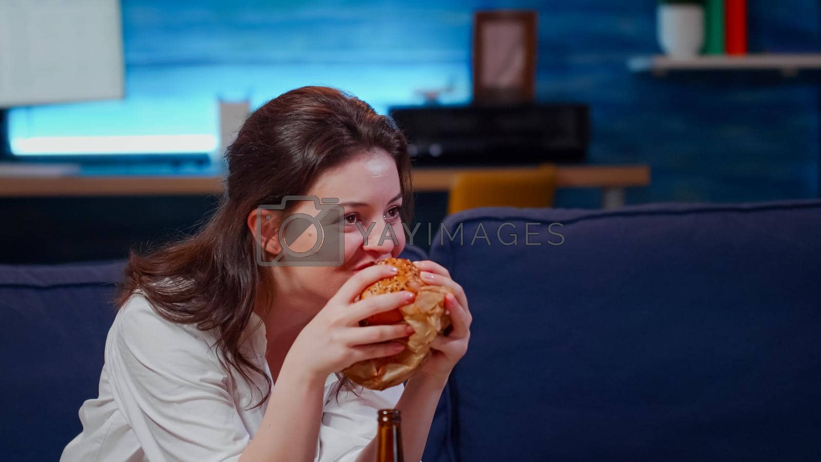 Royalty free image of Young person laughing at TV while eating hamburger by DCStudio