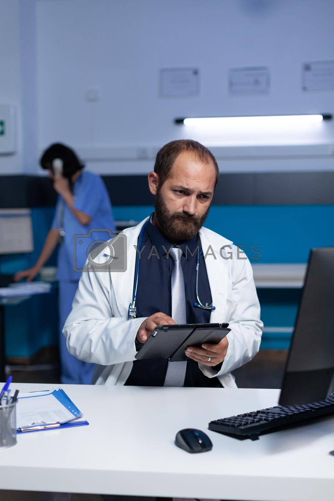 Practitioner using technology for healthcare system and medical practice at office. Doctor looking at digital tablet and computer screen for checkup information, working late at night