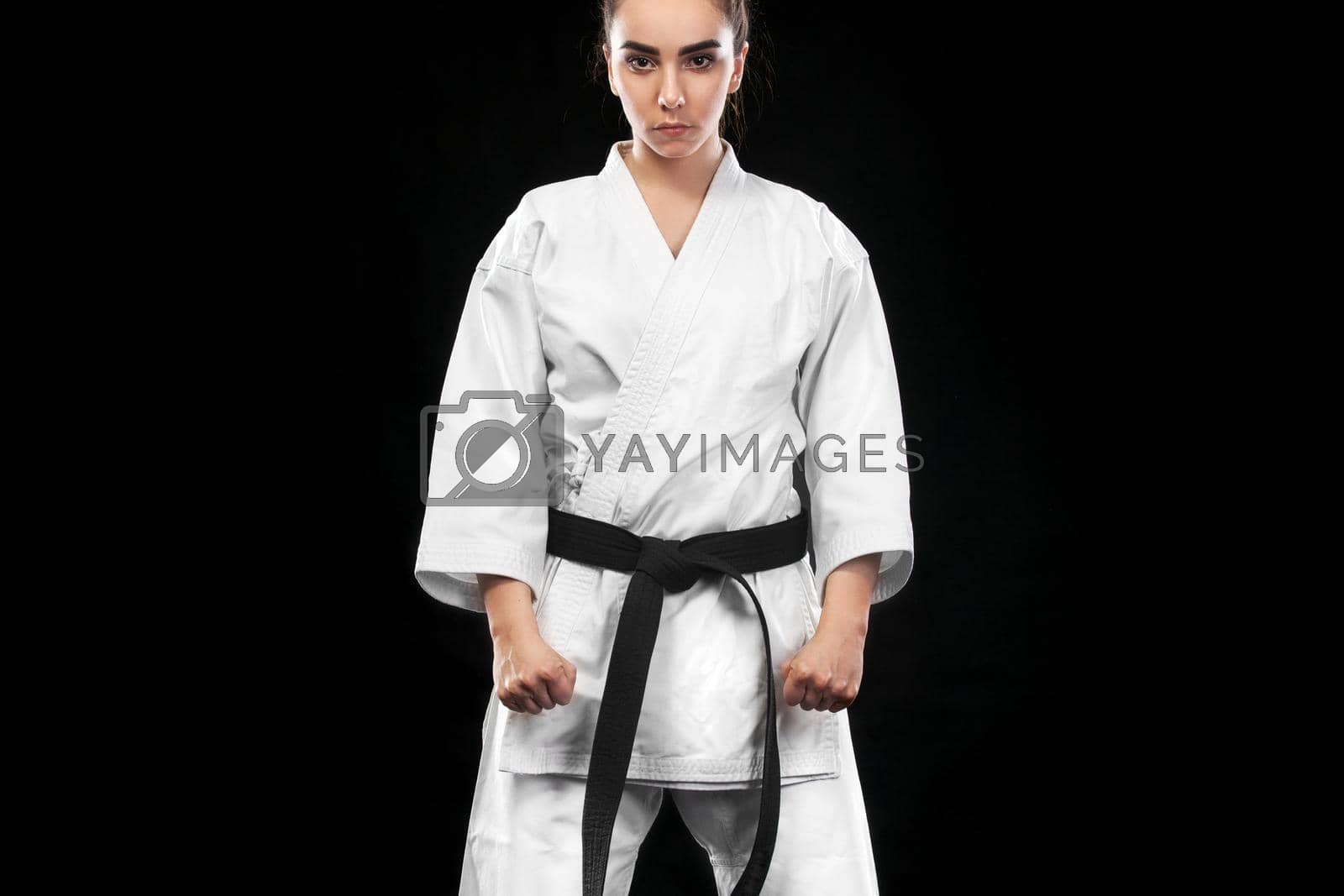 Royalty free image of Portrait of sporty karate and taekwondo woman in white kimono with black belt on dark background. by MikeOrlov