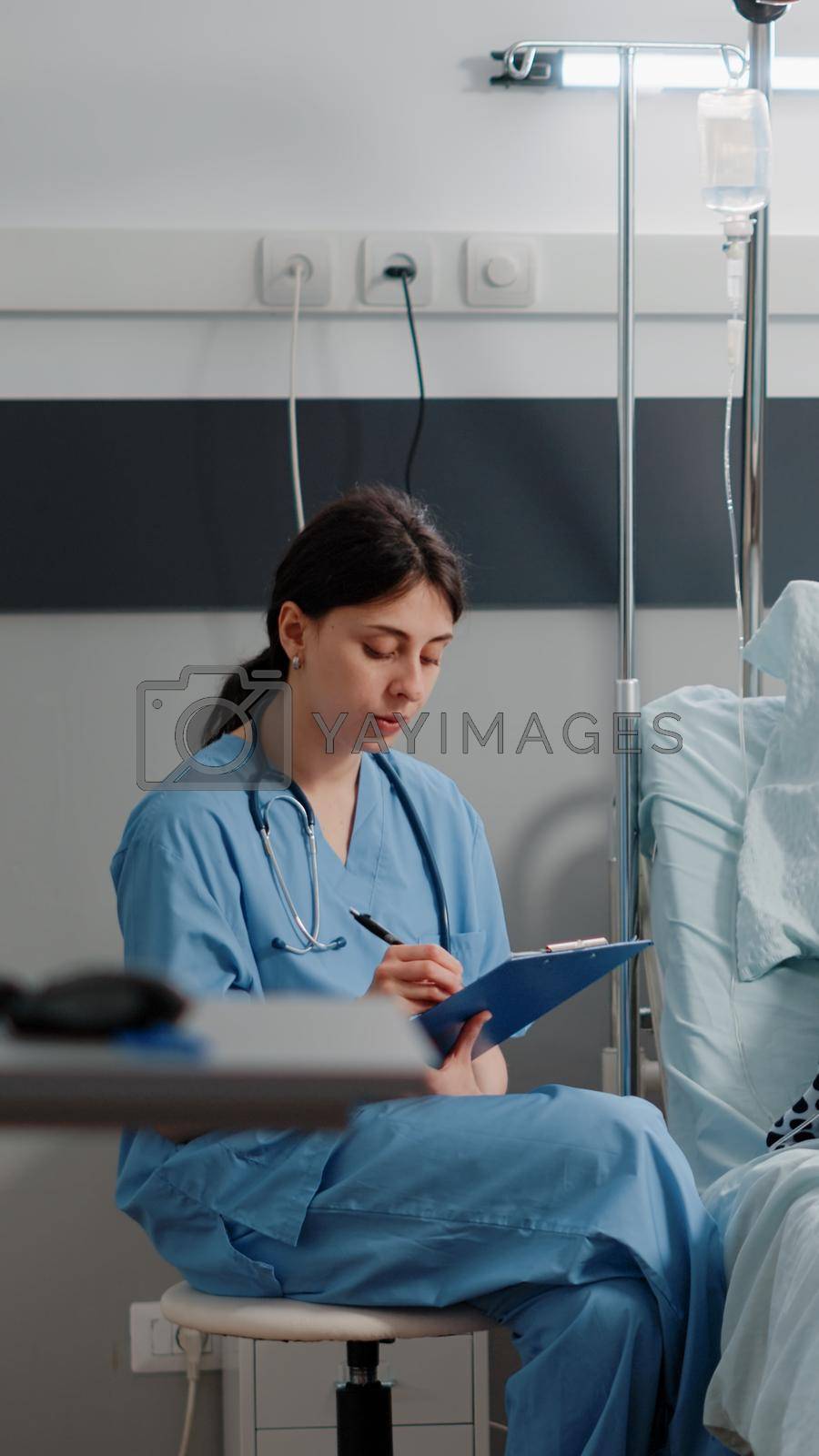 Medical assistant doing checkup visit with ill patient for healthcare and recovery. Nurse talking to aged woman with IV drip bag and nasal oxygen tube while taking notes for diagnosis
