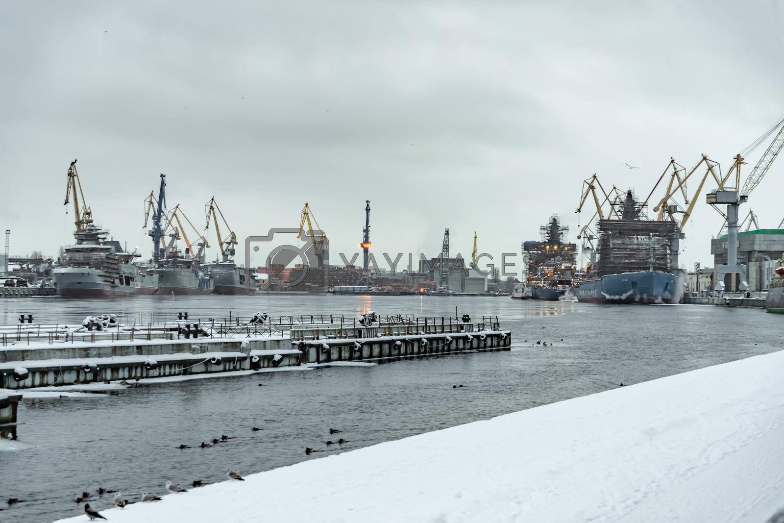 Russia, St. Petersburg, 05 February 2021: The construction of nuclear icebreakers, cranes of of the Baltic shipyard in a frosty winter day, steam over the Neva river, smooth surface of the river. High quality photo