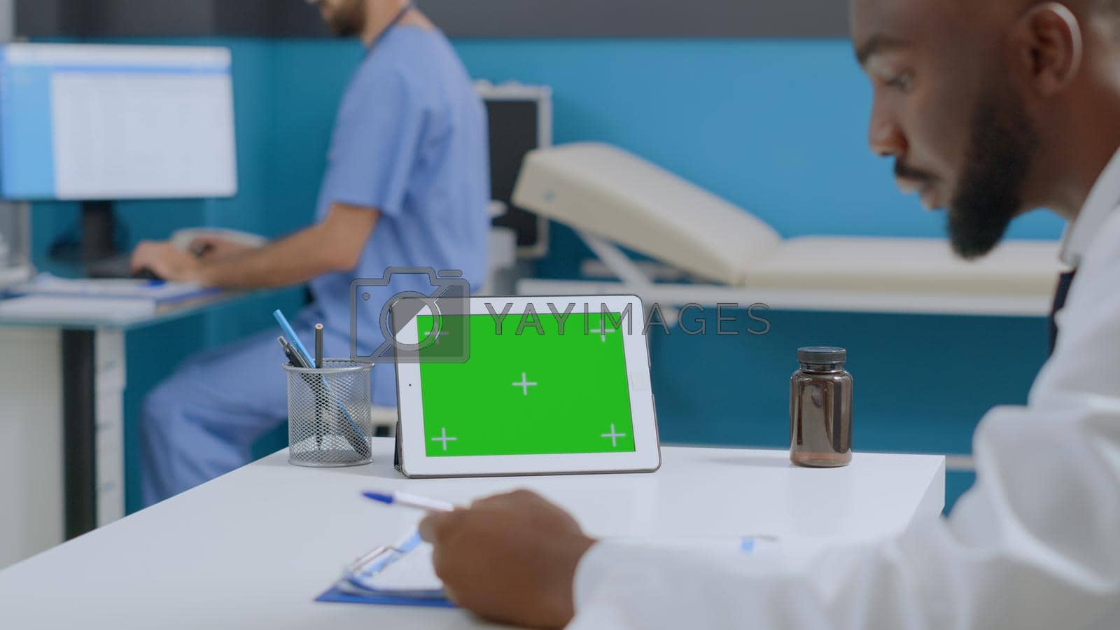African american physician doctor analyzing healthcare treatment document working at medical expertise in hospital office. Mock up green tablet computer with isolated display. Medicine services