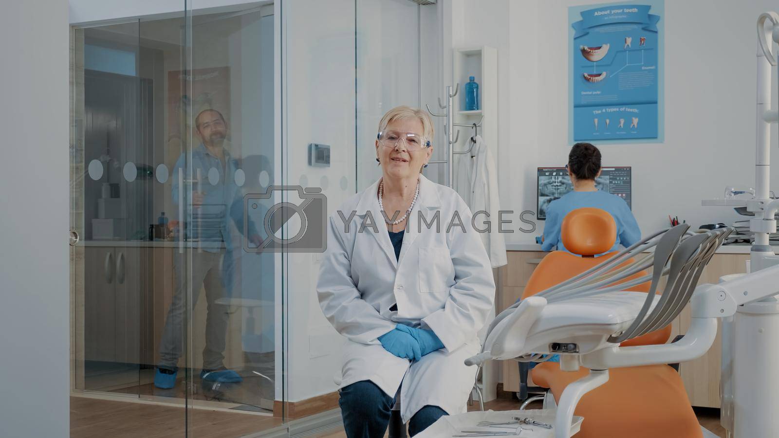 Portrait of dentist with glasses sitting in stomatology office, looking at camera. Dentistry expert getting ready to consult patient, working with dental equipment at oral care clinic.