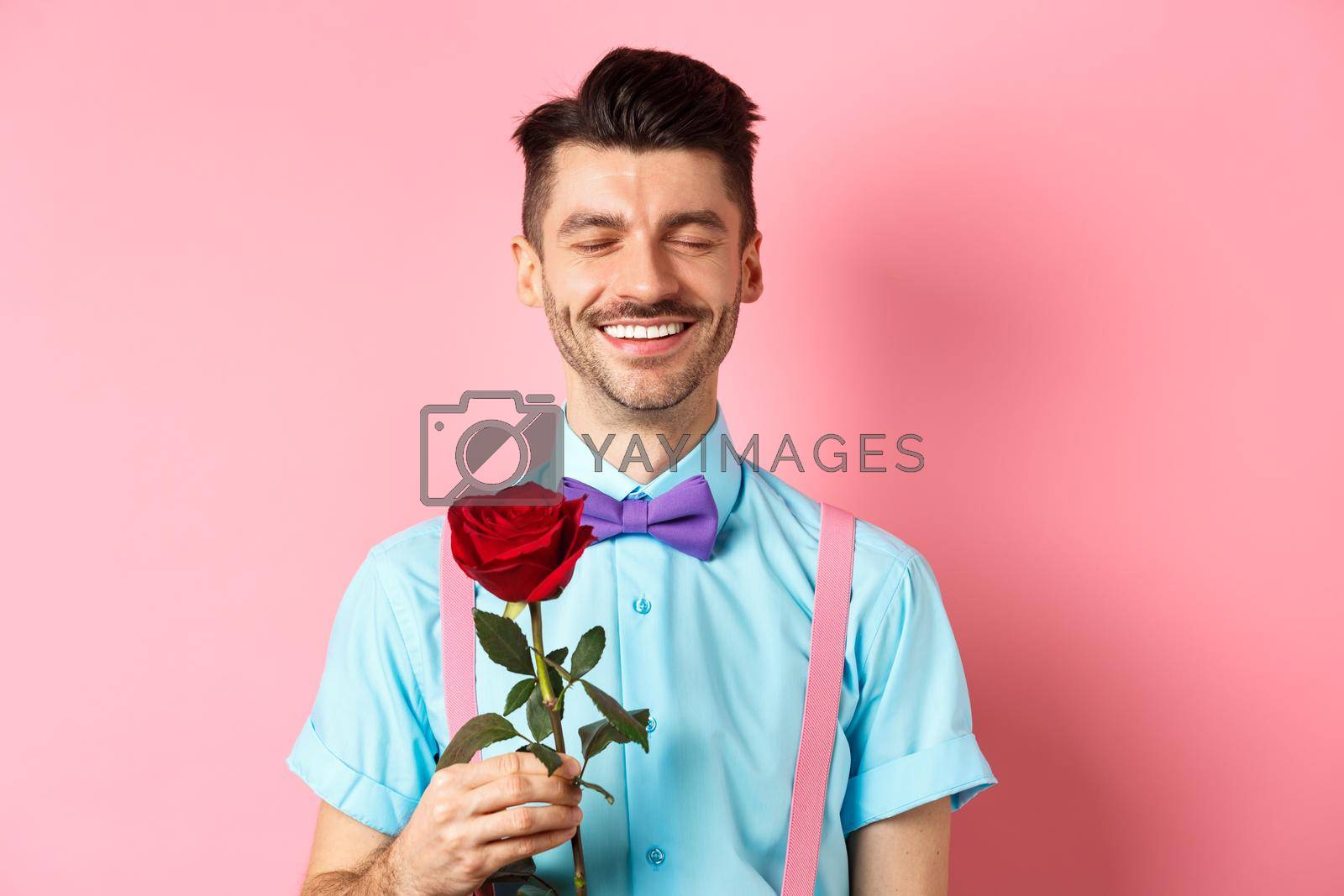 Valentines day and romance concept. Romantic man with red rose going on date with lover, standing in fancy bow-tie on pink background.