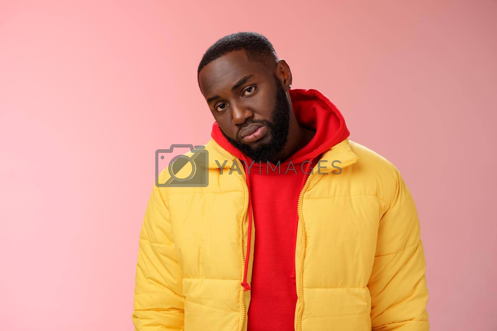Royalty free image of Unimpressed bored ignorant young african bearded man tilt head look scorn uninterest camera listen boring useless information, standing careless in yellow jacket red hoodie, indifferent by Benzoix