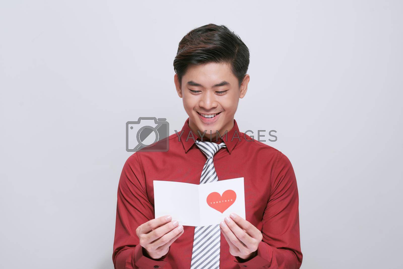 Handsome man with greeting card on light background. Valentine's Day celebration