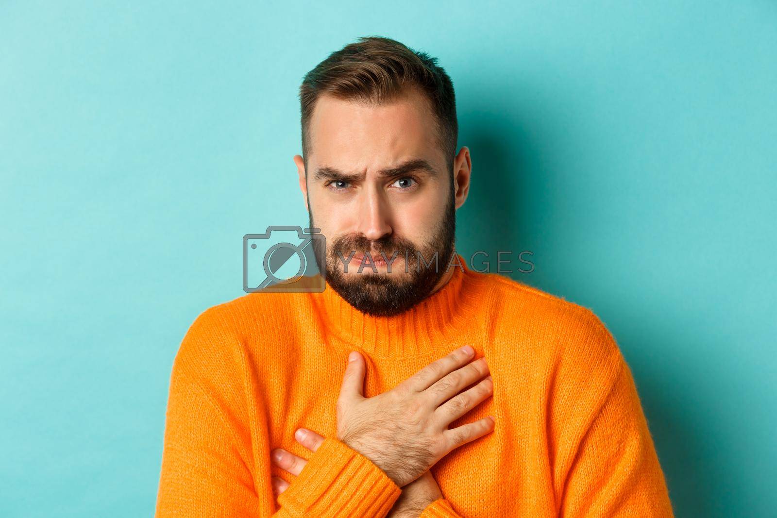 Royalty free image of Close-up of shocked and startled man touching chesk, looking displeased and worried, standing against light blue background by Benzoix