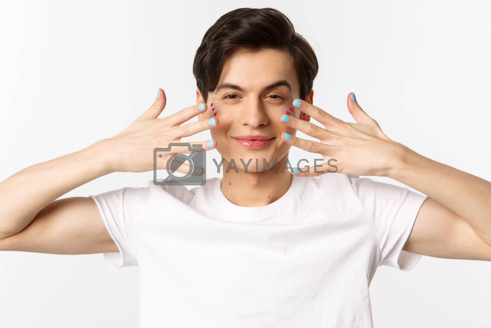 Royalty free image of People, lgbtq and beauty concept. Close-up of beautiful gay man with glitter on face, showing nail polish on his fingernails, looking sassy at camera, standing over white background by Benzoix