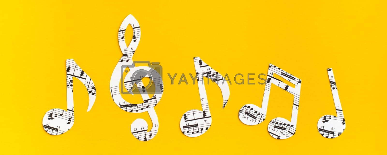 Royalty free image of Musical notes and clef cut from paper with musical text in a row on yellow background. Web banner by Aleruana