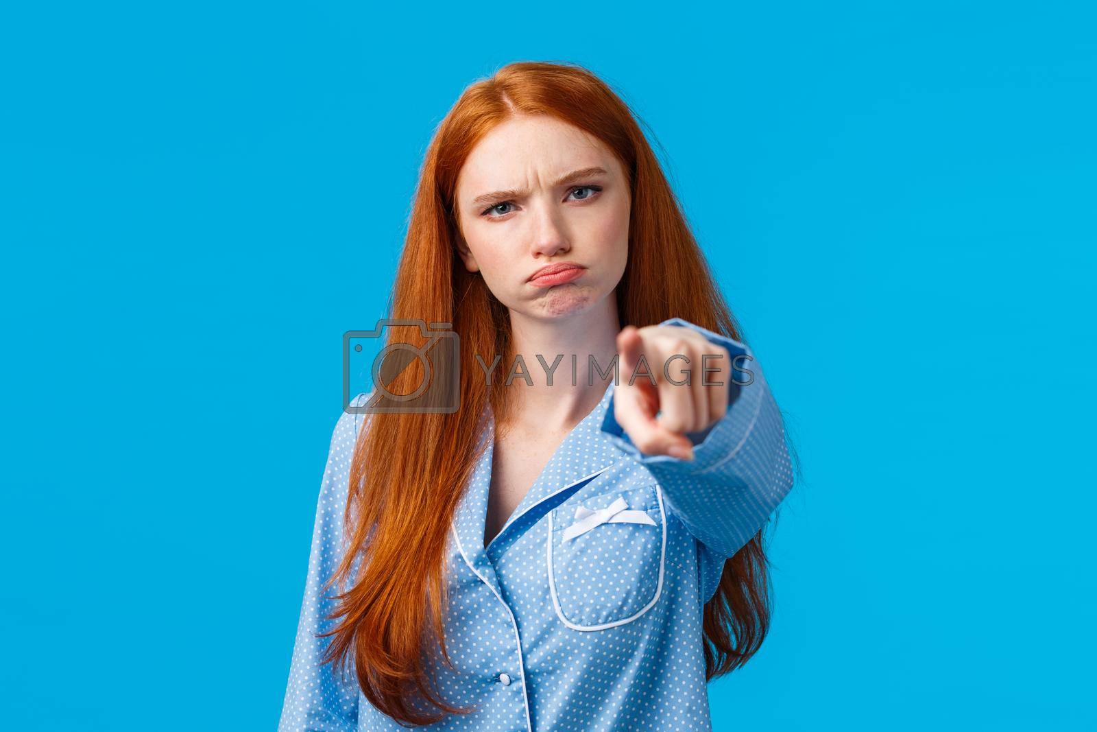 Royalty free image of Offended timid and silly redhead teenager, girl in nightwear pointing at camera with blame, shame someone, sulking and frowning angry, accuse person, standing blue background unsatisfied by Benzoix