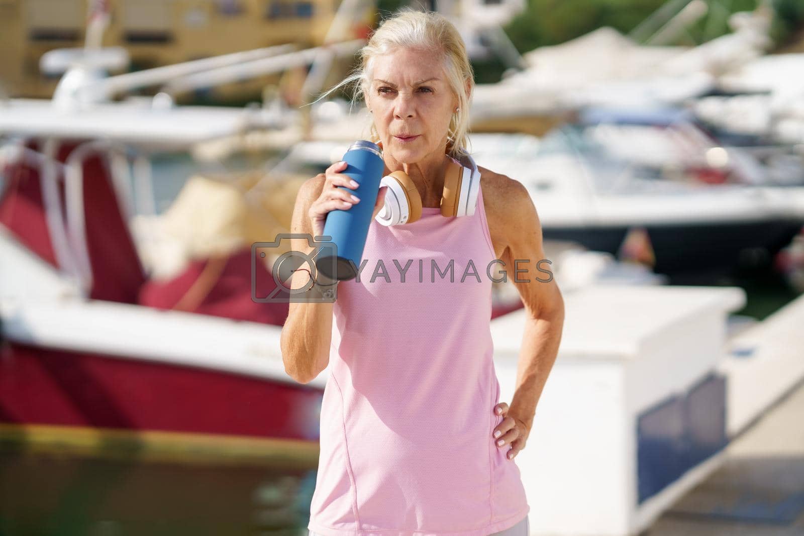 Mature sportswoman taking a break during exercise to hydrate herself. Senior woman in fitness clothing drinking water from a metal fitness bottle. Concept of healthy living in the elderly.